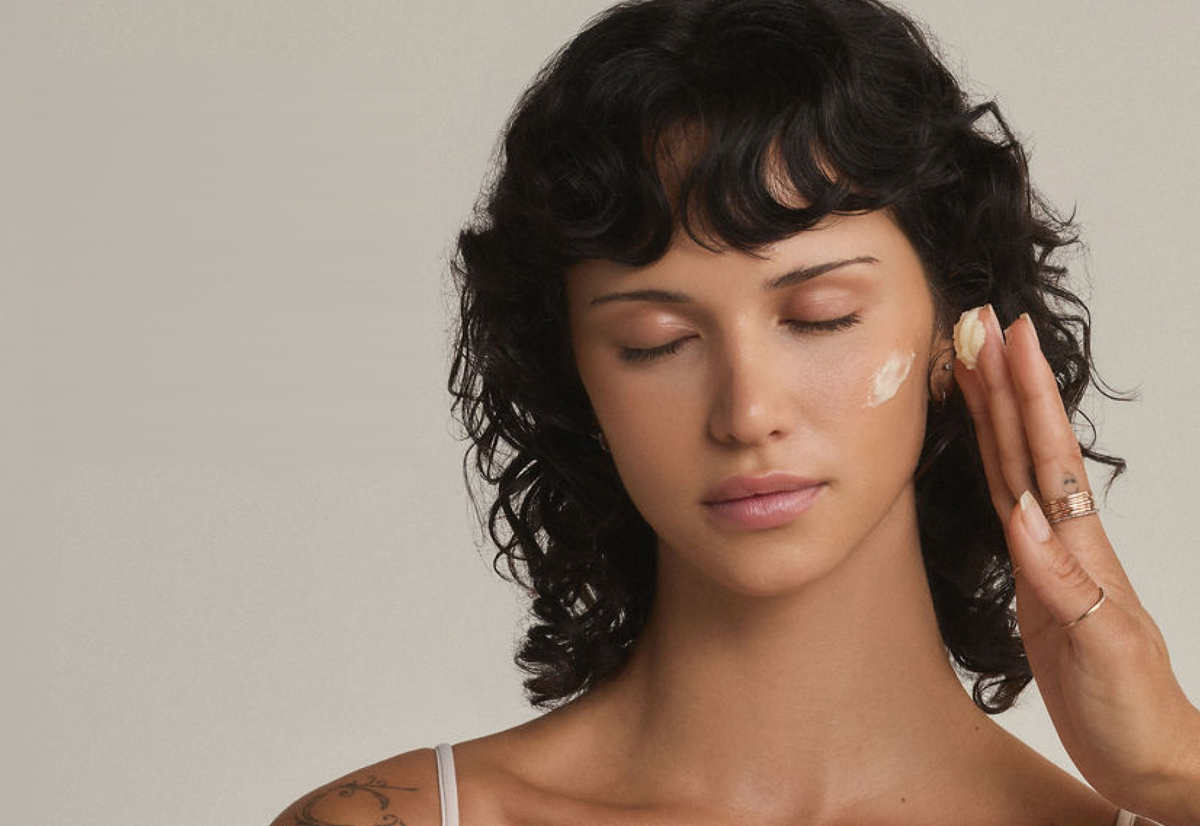 Woman with eyes closed applying TALOVA Face + Body Balm to her cheek